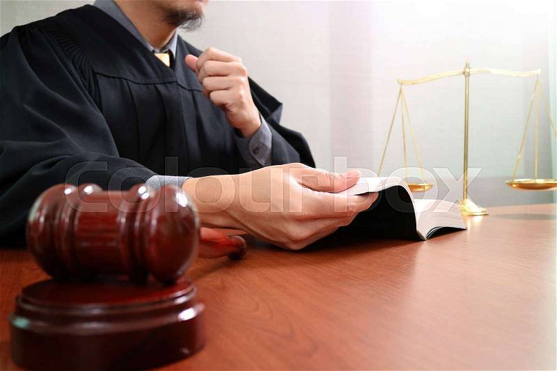 Justice and law concept.Male judge in a courtroom with the gavel,opening holy book and digital tablet computer with brass scale on wood table , stock photo