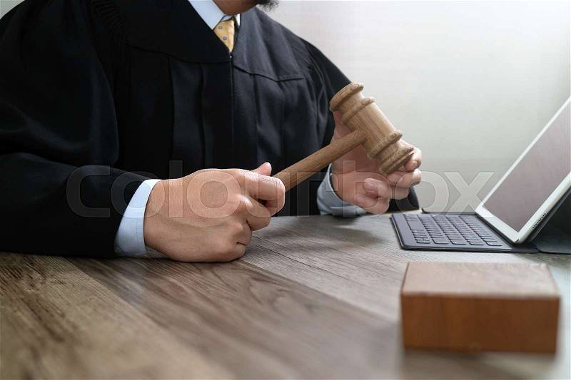 Justice and law concept.Male judge in a courtroom with the gavel,working with digital tablet computer docking keyboard on wood table, stock photo
