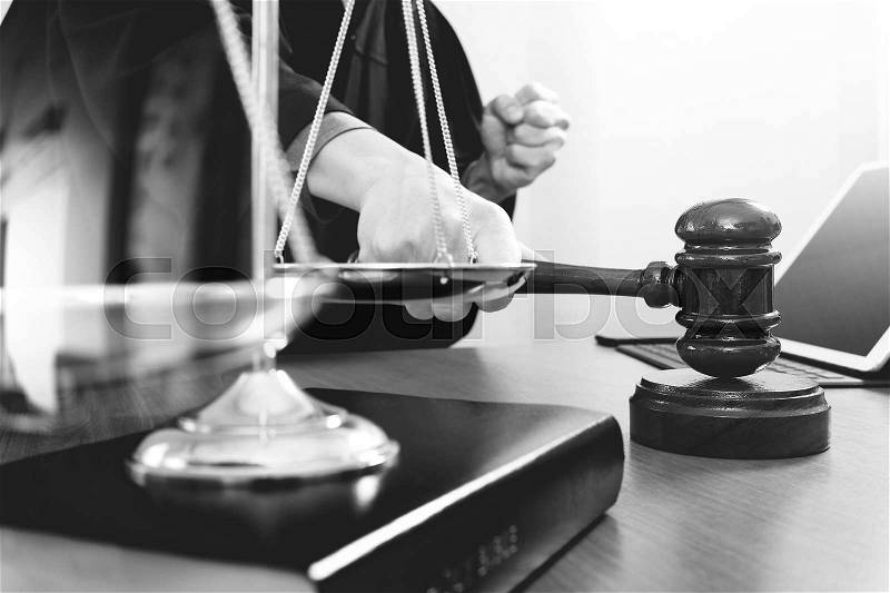 Justice and law concept.Male judge in a courtroom with the gavel,working with smart phone and digital tablet computer with brass scale on wood table,black and white , stock photo