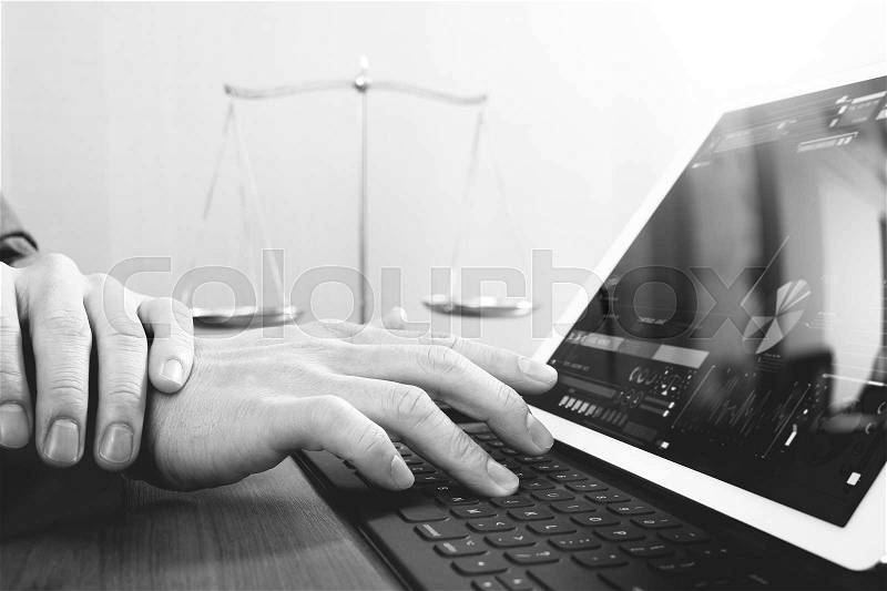Justice and law concept.Male lawyer in office with the gavel,working with smart phone and digital tablet computer and brass scale on wood table,black and white, stock photo