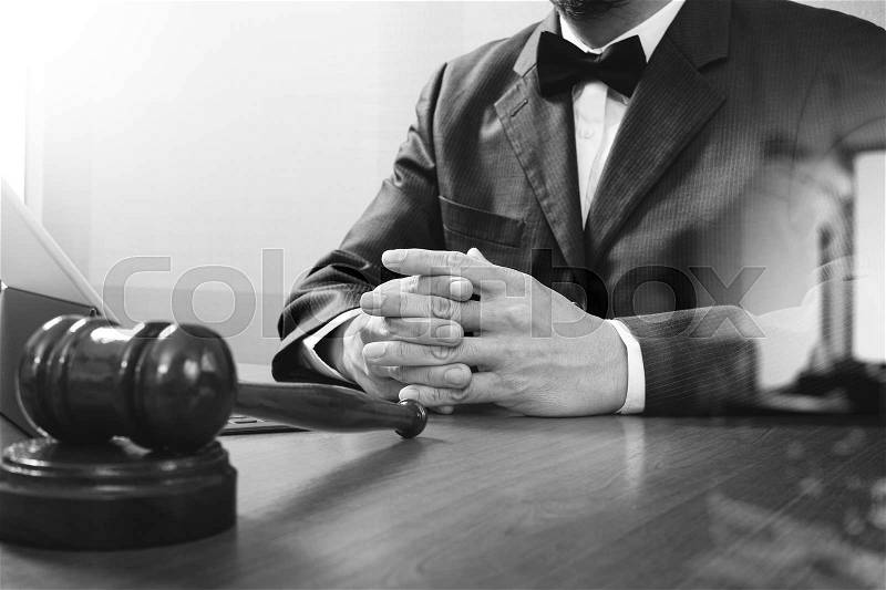 Justice and law concept.Male judge in a courtroom with the gavel,working with smart phone,digital tablet computer docking keyboard,eyeglasses,on wood table,black and white, stock photo