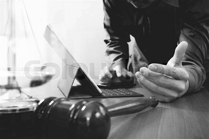 Justice and law concept.Male lawyer in office with the gavel,working with smart phone and digital tablet computer and brass scale on wood table,black and white, stock photo