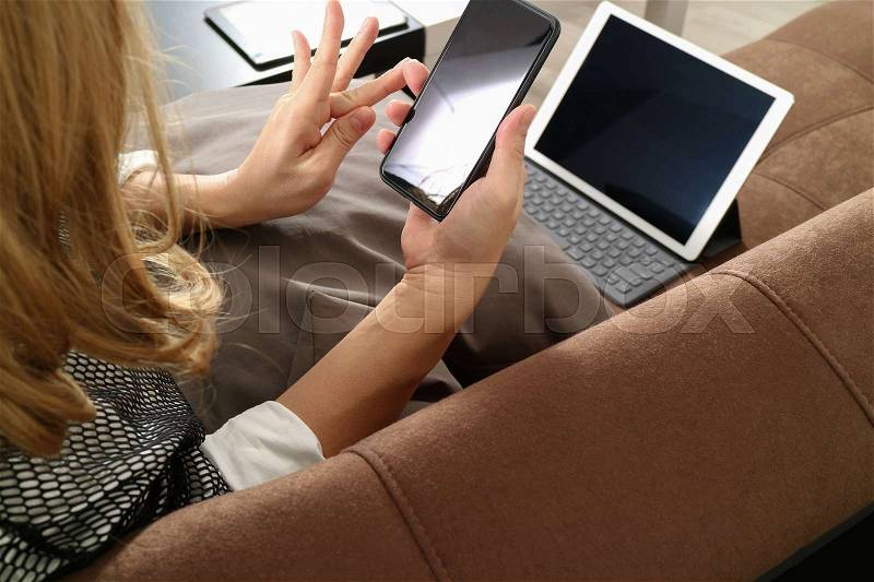 Brunette woman using smart phone and digital tablet computer on sofa in living room, stock photo