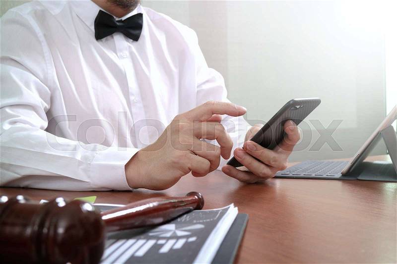 Justice and Law context.Male lawyer hand working with smart phone,digital tablet computer docking keyboard with gavel and document on wood table, stock photo