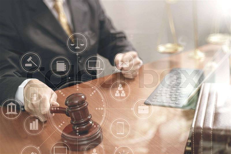 Justice and law concept.Male judge in a courtroom with the gavel,working with smart phone,digital tablet computer docking keyboard,brass scale,on wood table,virtual interface graphic icons diagram, stock photo