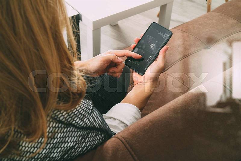 Brunette woman using smart phone and digital tablet computer on sofa in living room, stock photo