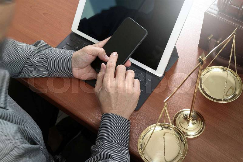 Justice and law concept.Male lawyer in office with the gavel,working with smart phone,digital tablet computer docking keyboard,brass scale,on wood table, stock photo