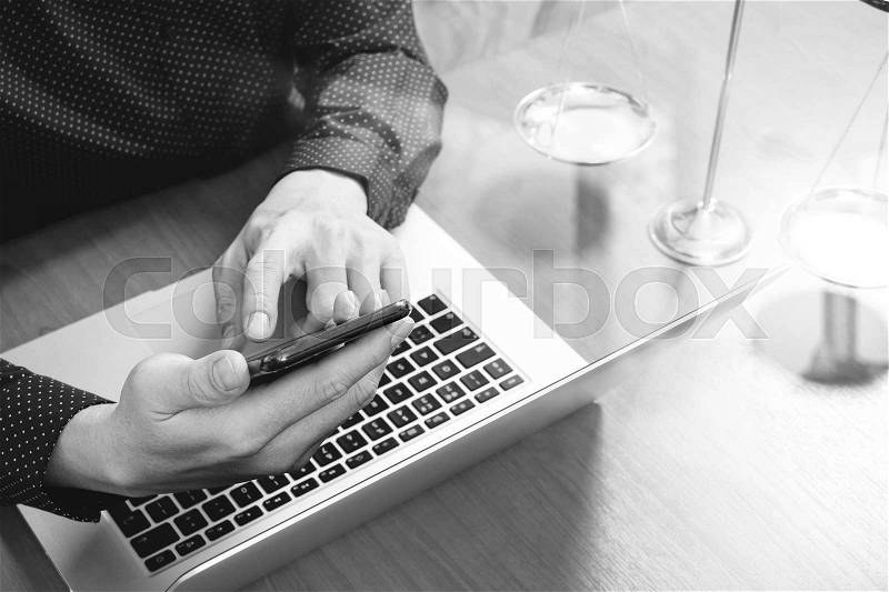 Justice and law concept.Male lawyer in office with the gavel,working with smart phone,digital tablet computer docking keyboard,brass scale,on wood table,black and white, stock photo