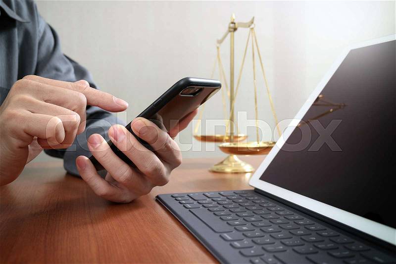 Justice and law concept.Male lawyer in office with the balance brass scale,hand working with smart phone and digital tablet computer on wooden desk, stock photo