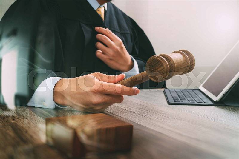 Justice and law concept.Male judge in a courtroom with the gavel,working with digital tablet computer docking keyboard on wood table,filter effect, stock photo
