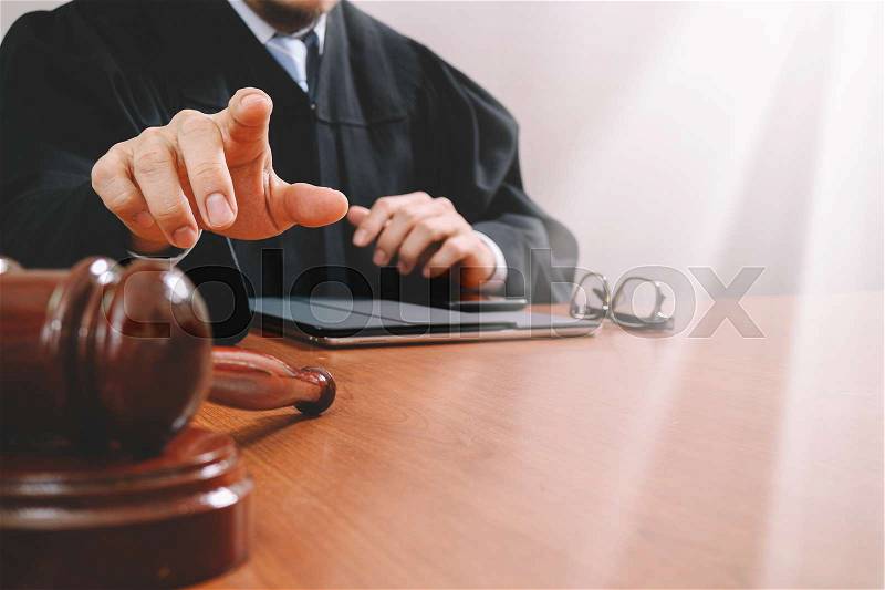 Justice and law concept.Male judge in a courtroom with the gavel,working with smart phone,digital tablet computer docking keyboard,eyeglasses,on wood table,filter, stock photo