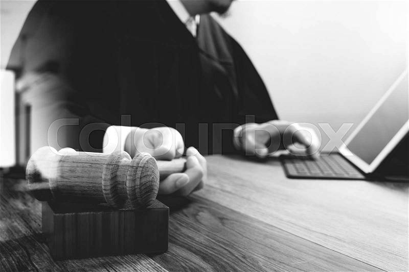 Justice and law concept.Male judge in a courtroom with the gavel,working with smart phone,digital tablet computer docking keyboard on wood table,black and white, stock photo