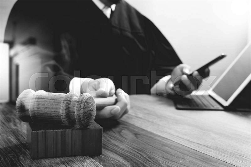 Justice and law concept.Male judge in a courtroom with the gavel,working with digital tablet computer docking keyboard on wood table,black and white, stock photo