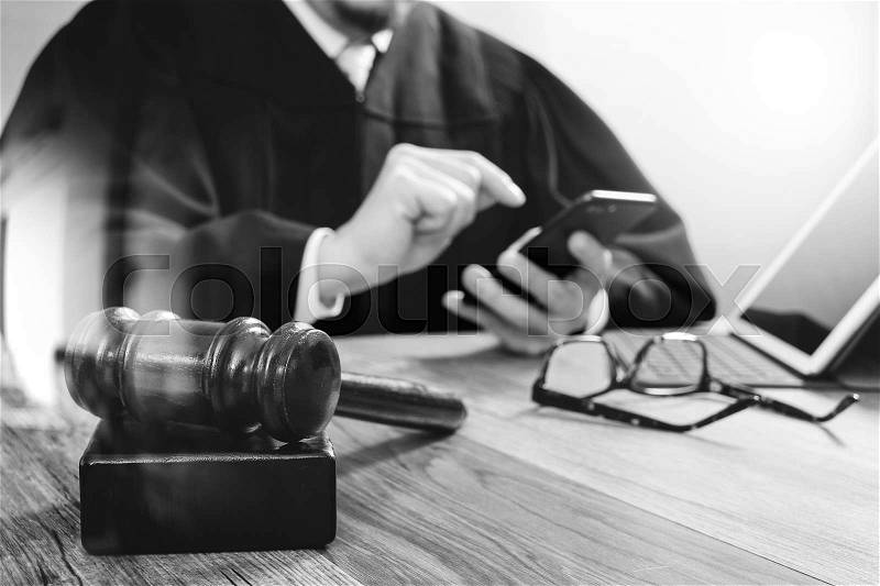 Justice and law concept.Male judge in a courtroom with the gavel,working with smart phone,digital tablet computer docking keyboard on wood table,black and white, stock photo