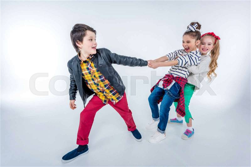 Side view of laughing girls pulling up boy on grey, stock photo
