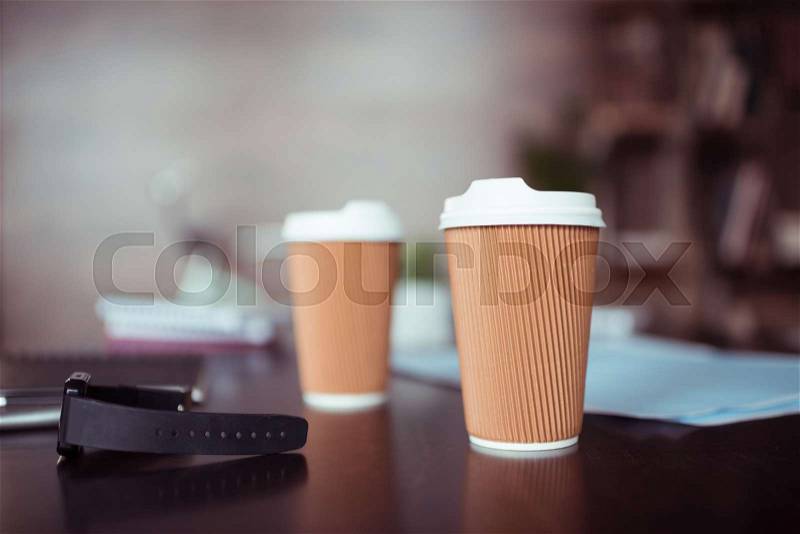 Close-up view of smartwatch and disposable coffee cups on table, stock photo