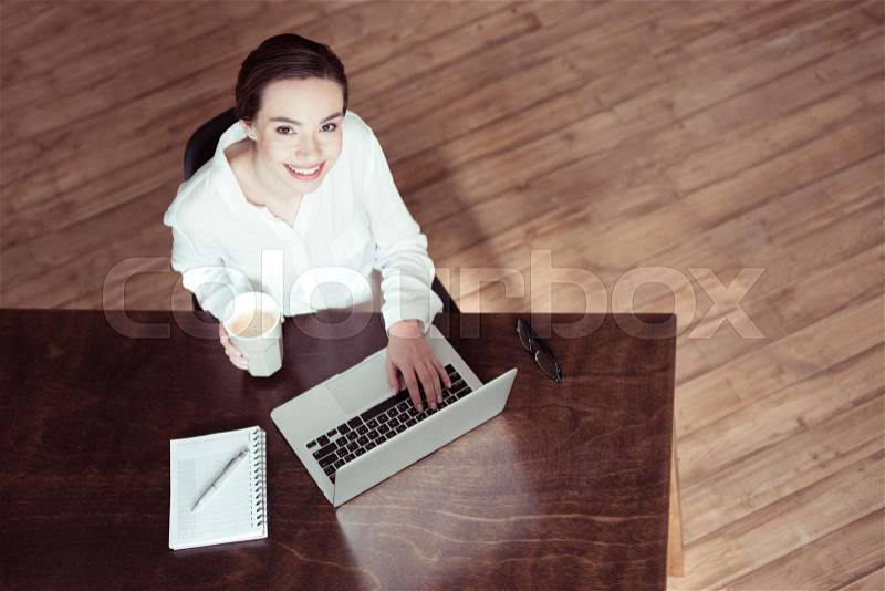Businesswoman using laptop and looking at camera in office, stock photo