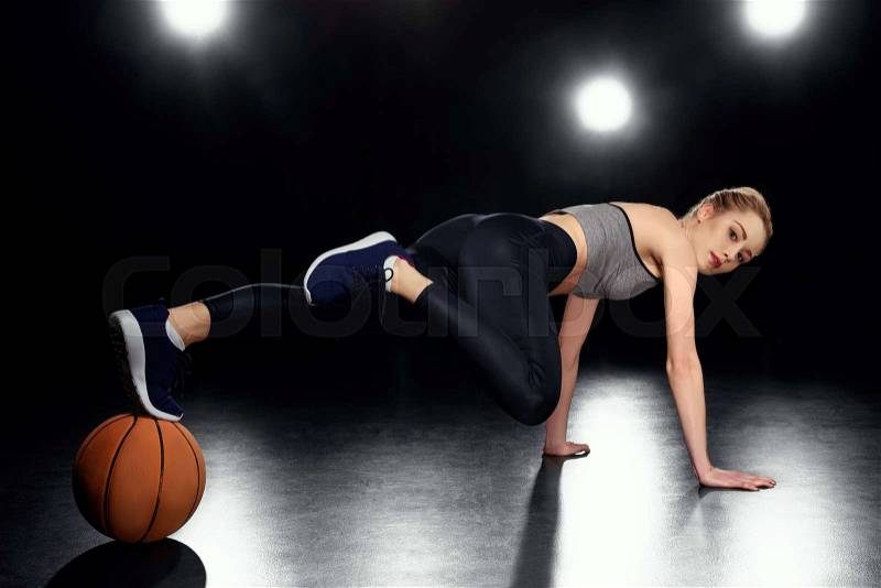 Attractive sportswoman in plank position with basketball ball on black, stock photo