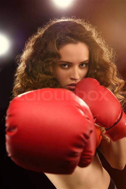 Beautiful young sportswoman in boxing gloves punching at camera, stock photo