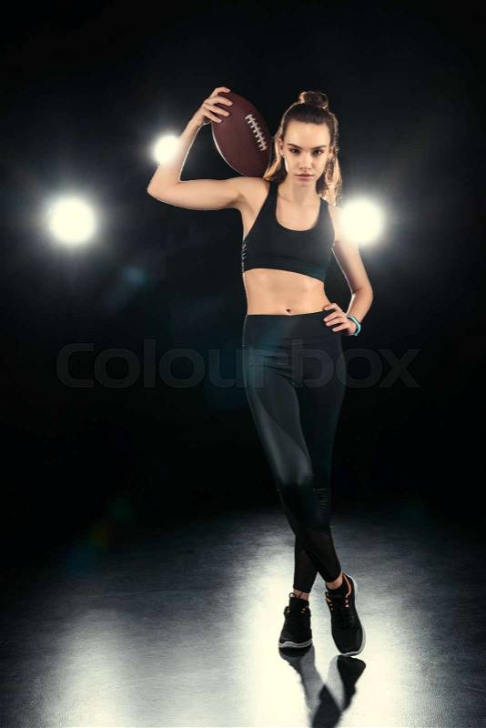 Confident young woman in sportswear holding rugby ball on shoulder, stock photo