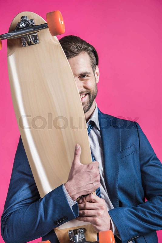 Portrait of man in suit holding skateboard on pink, stock photo