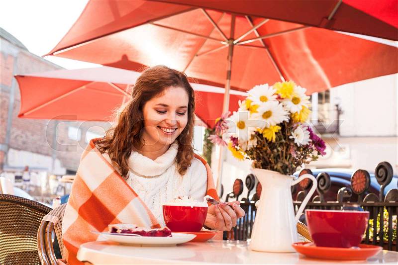 Woman is sitting in cafe outdoor and eat cake and cocoa, cozy autumn, stock photo