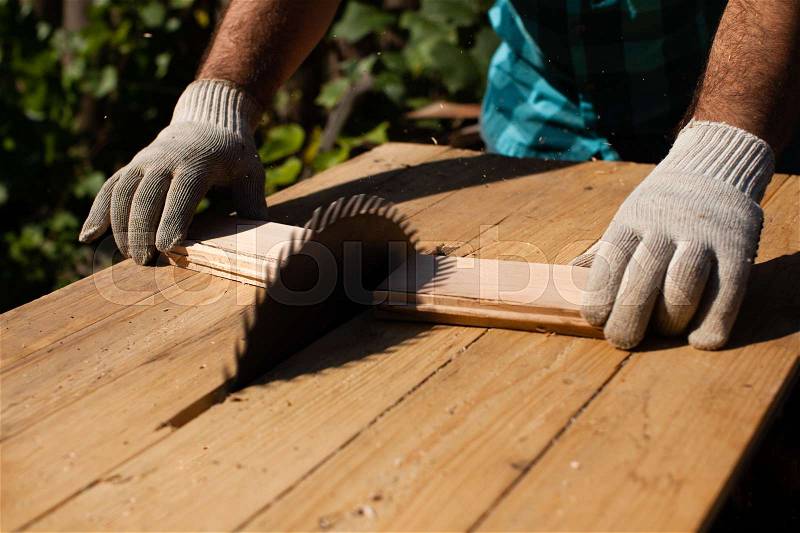 Hard working woodworker cutting wooden plank, focus on saw, stock photo