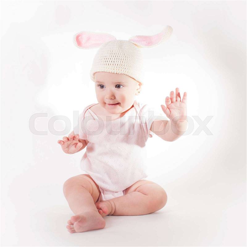 Cute baby girl sitting in a knitted rabbit hat isolated on white, stock photo