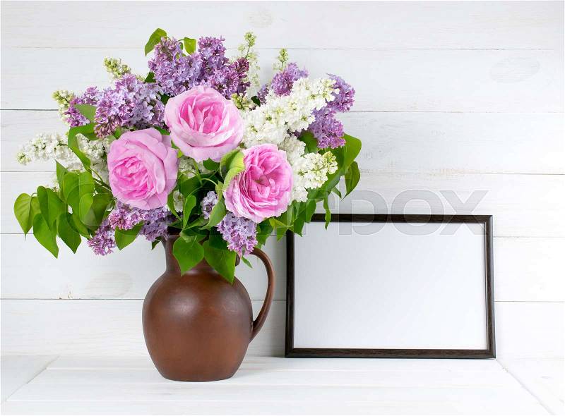 Lilac and roses in clay jug with motivational frame for your text or picture on background of white wooden planks in scandinavian style, stock photo