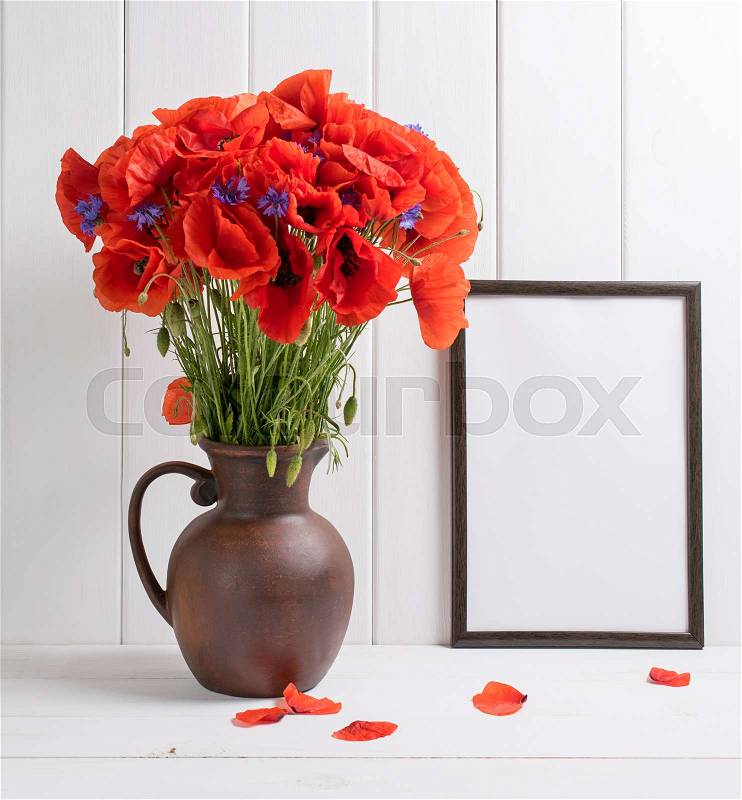 Red poppies bouquet in clay jug with motivational frame for your text or picture on background of white wooden planks in scandinavian style, stock photo