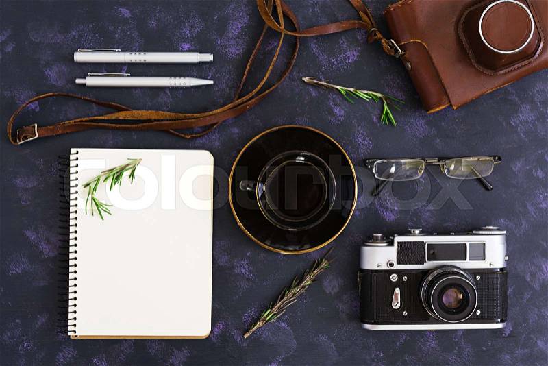 Flat lay, top view office table desk. Desk workspace with retro camera, diary, pen, glasses, case, cup of coffee, rosemary on dark background, stock photo