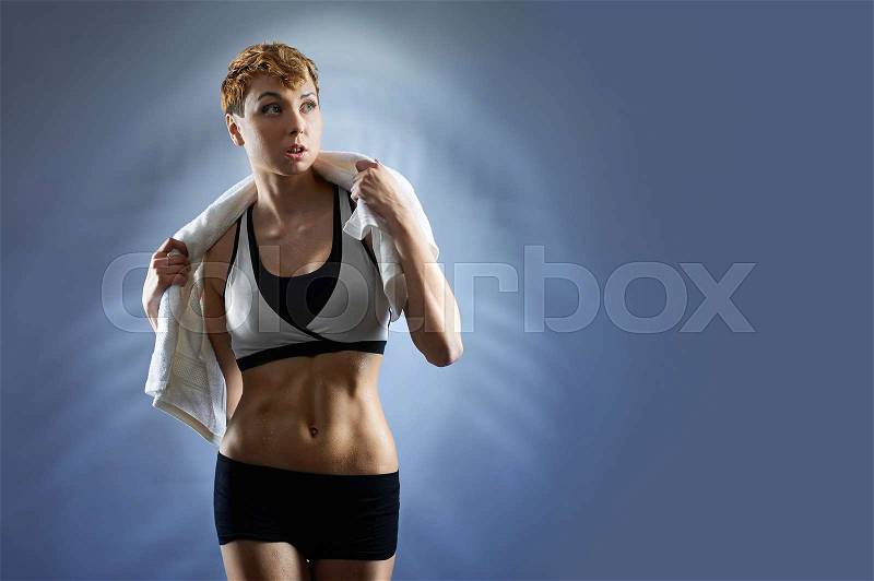Feeling fit. Female fitness trainer wearing sports clothing posing with a towel around her neck on blue background looking away copyspace on the side, stock photo