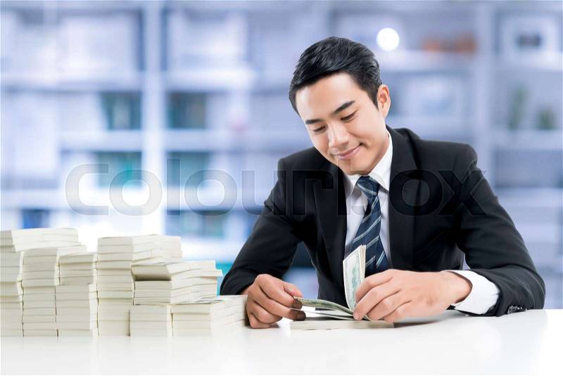 The young banker is smiling and counting banknotes and a big pile of money on the white table on bank office background, concept business and financial. , stock photo