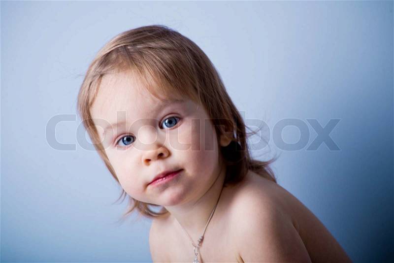Nice baby girl looking into camera on blue background, stock photo