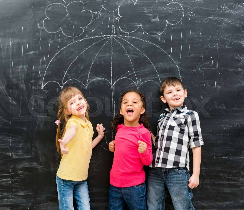 Three funny children standing under drawn on blackboard umbrella , stock photo
