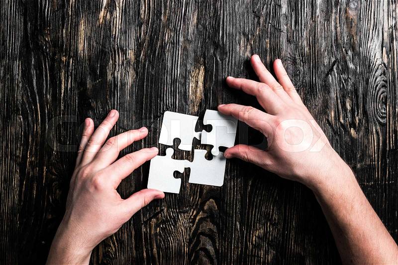 Hands with pieces of white jigsaw on dark wooden table, stock photo