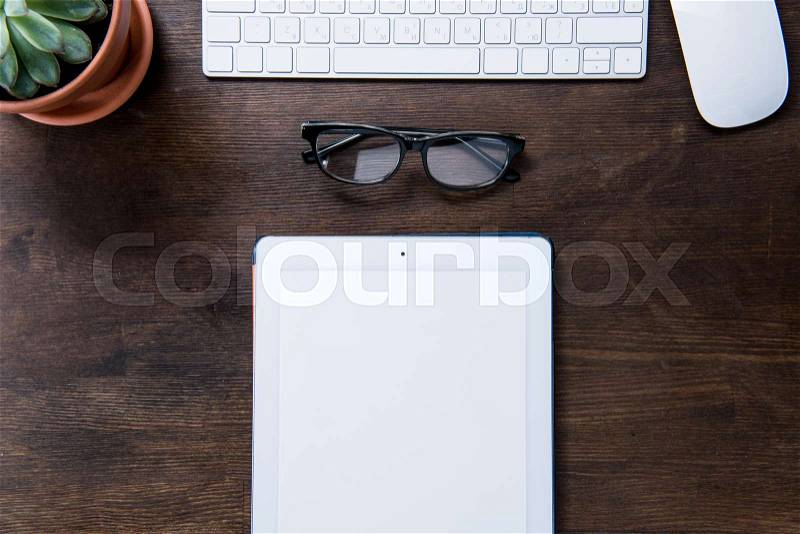 Top view of digital tablet, eyeglasses, computer mouse and keyboard on office desk, stock photo