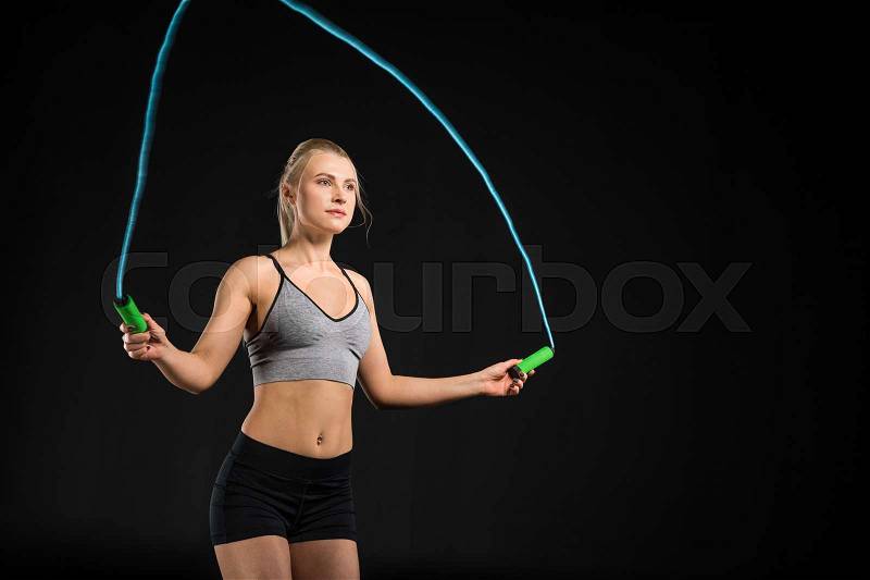 Attractive young woman in sportswear exercising with skipping rope on black, stock photo