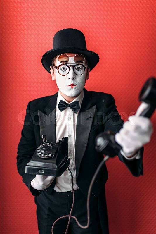 Mime theater actor performing with old telephone. Comedy pantomime artist in suit, gloves and hat, stock photo