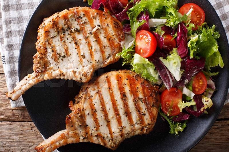 Grilled pork steak with bone, fresh vegetable salad close-up on plate. horizontal view from above , stock photo