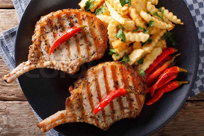 Grilled pork steak with bone, chili pepper and fries close-up on plate. Horizontal view from above , stock photo