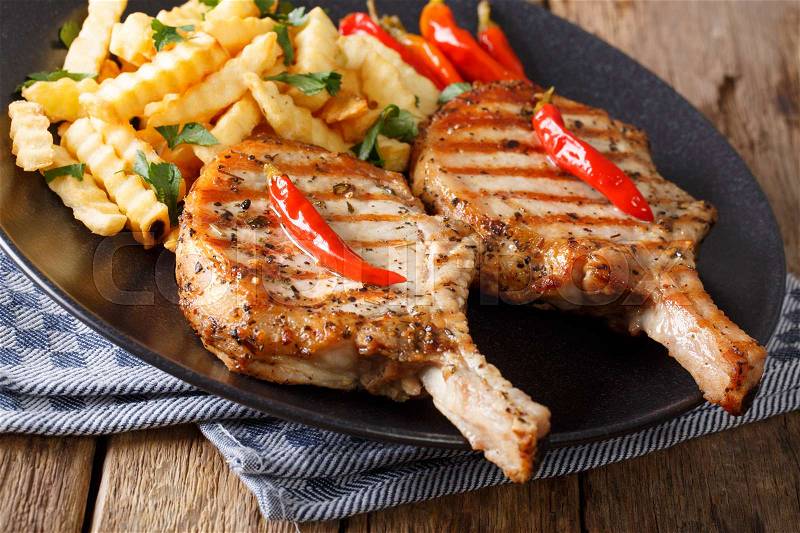 Barbecue spicy pork chop with chili and french fries close-up on a plate on a table. horizontal , stock photo