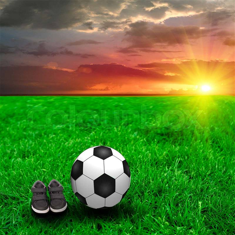 A soccer ball and baby\'s trainers on green grass in the sunset, stock photo