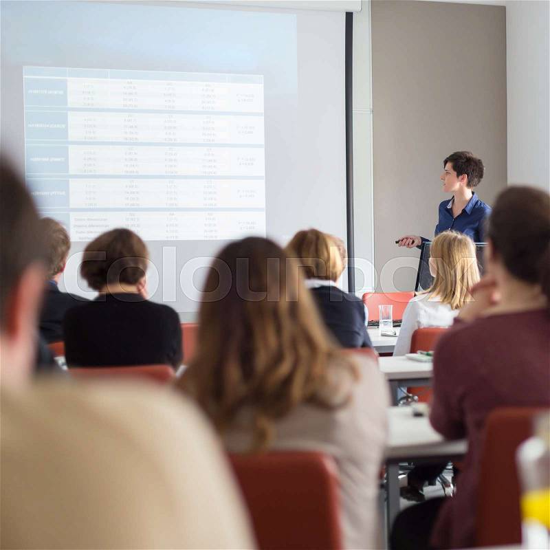 Female speaker giving presentation in lecture hall at university workshop . Participants listening to lecture and making notes. Scientific conference event, stock photo