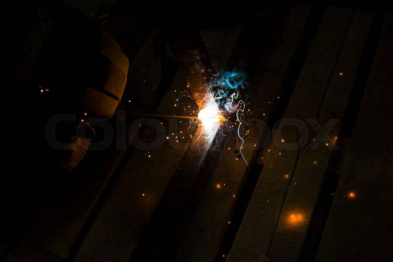 Worker with personal protective equipment and protective mask welding steel pipe in factory, stock photo