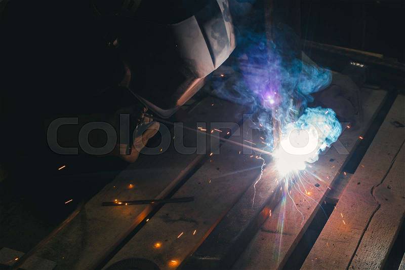 Worker with personal protective equipment and protective mask welding steel pipe in factory, stock photo