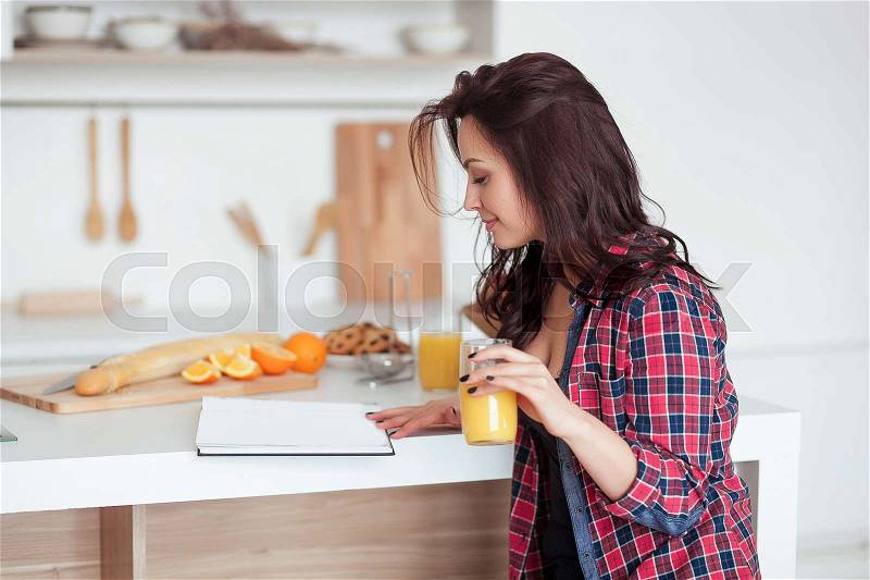 Breakfast - Smiling woman reading book in white kitchen, fresh orange juice. Health Care And Beauty Concept, stock photo