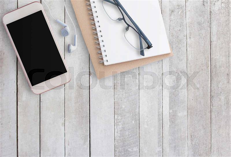 Blank notebooks,glasses and smart phone with earphone on white wood background. Top view with copy space (selective focus). Office desk table concept, stock photo