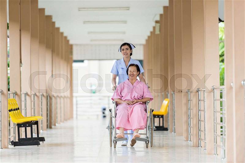 Happy nurse Carrying Senior woman Patient On Wheelchair, stock photo