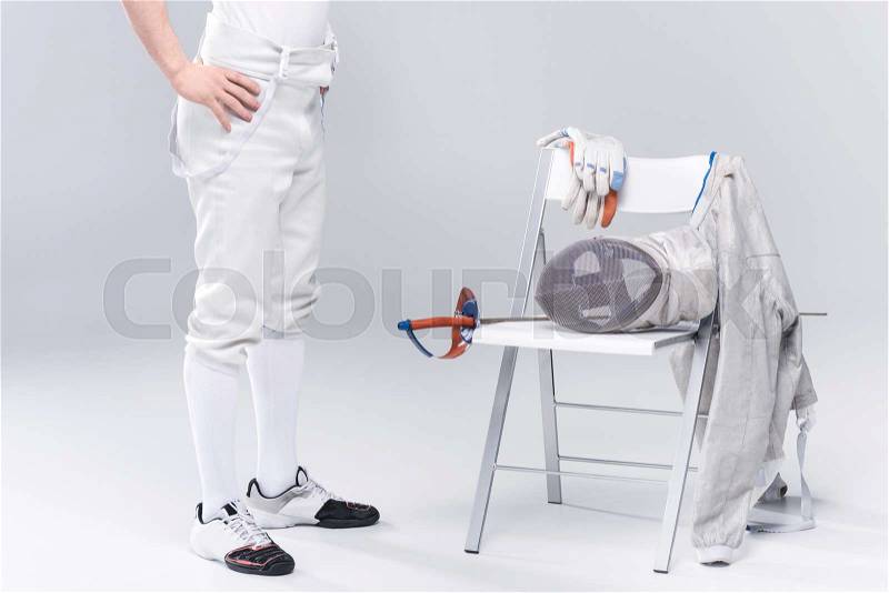 Low section of young man professional fencer standing near chair with fencing equipment, stock photo